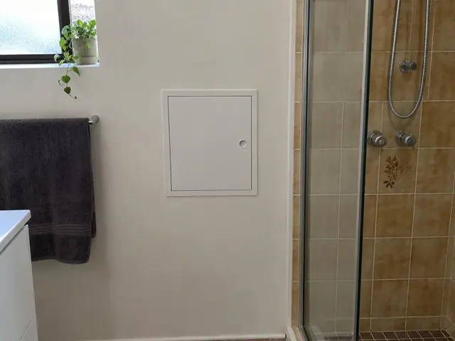 Bathroom wall with a small access panel beside a tiled shower and towel rail in Claremont Meadows